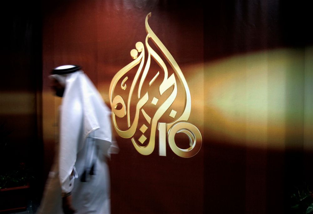 A Qatari employee of Al Jazeera Arabic language TV news channel walks past the logo of Al Jazeera in Doha, Qatar.