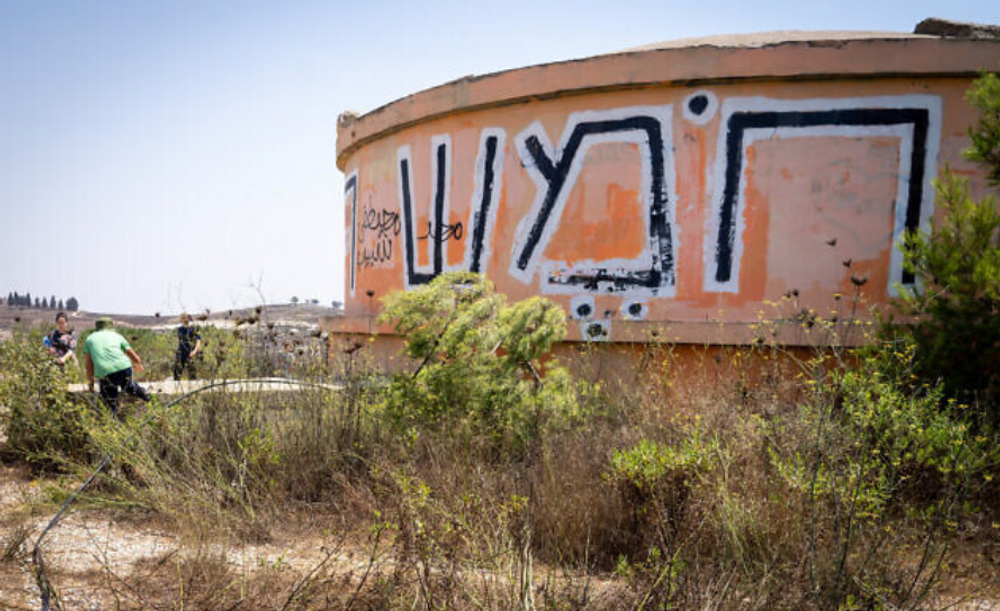 People walk near a water tower at Homesh Ruins, labelled with the word "Homesh" in Hebrew, in the northern West Bank, on August 27, 2019.