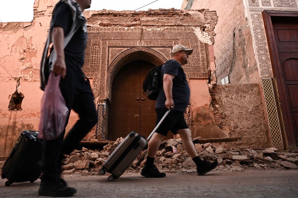 سياح يسحبون حقائبهم أمام مبنى متضرر في الأحياء القديمة بمدينة مراكش، 10 سبتمبر 2023، بعد يومين من الزلزال