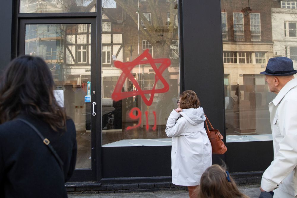 People look at antisemitic graffiti on a shop window in Belsize Park, North London, Dec. 29, 2019.