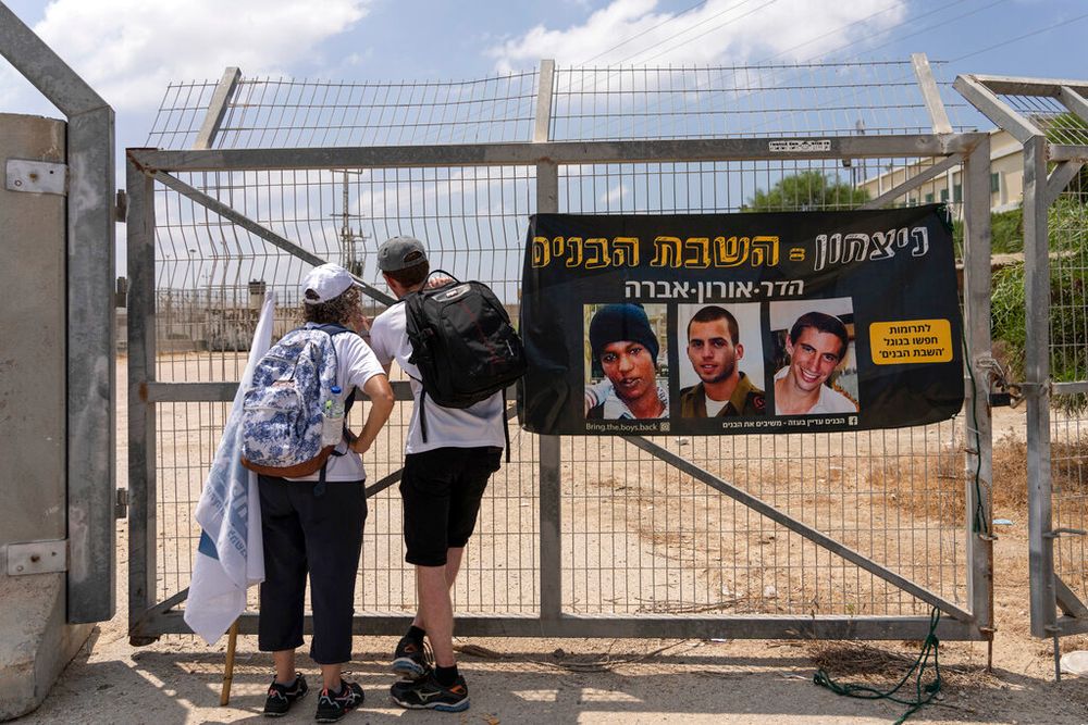 Israelis look towards the fence for the Erez border crossing on the Israel-Gaza border, next to a banner showing captive Israeli civilians Avera Mengistu (L) and late soldiers Oron Shaul (C) and Hadar Goldin.