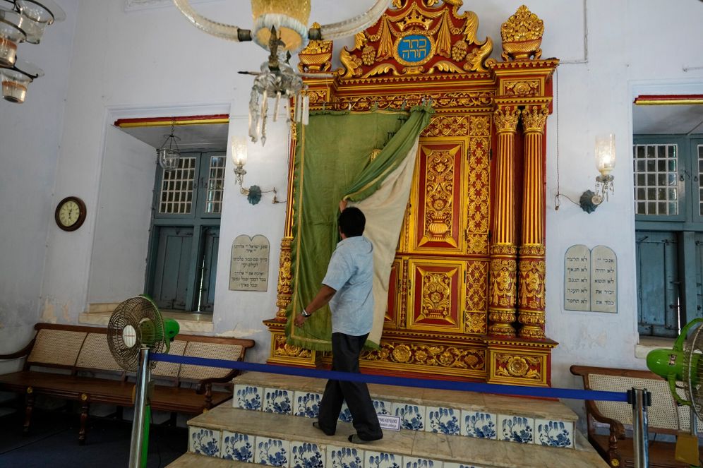 Synagogue trustee M.C. Praveen removes the ornate ceremonial curtain from the carved teakwood Torah ark, located on the western wall facing Jerusalem, at the 458-year-old Paradesi Synagogue in the historic Jew Town neighborhood of Kochi, India, Wednesday, May 20, 2026. 

