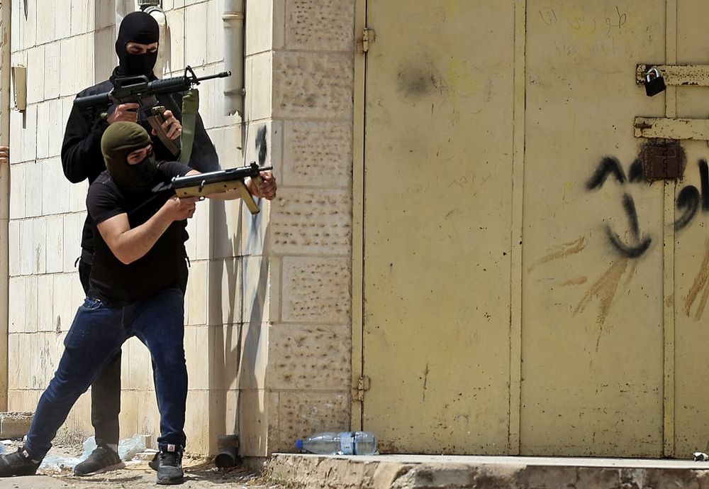 Masked Palestinian men hold automatic weapons during clashes with Israeli security forces in the West Bank city of Jenin, on May 13, 2022.