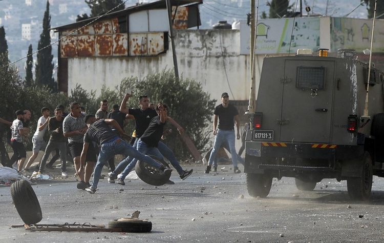 Palestinian youths throw stones at army vehicles during a military operation by the Israeli army to arrest wanted persons from the Balata camp near the West Bank city of Nablus, on August 17, 2022.