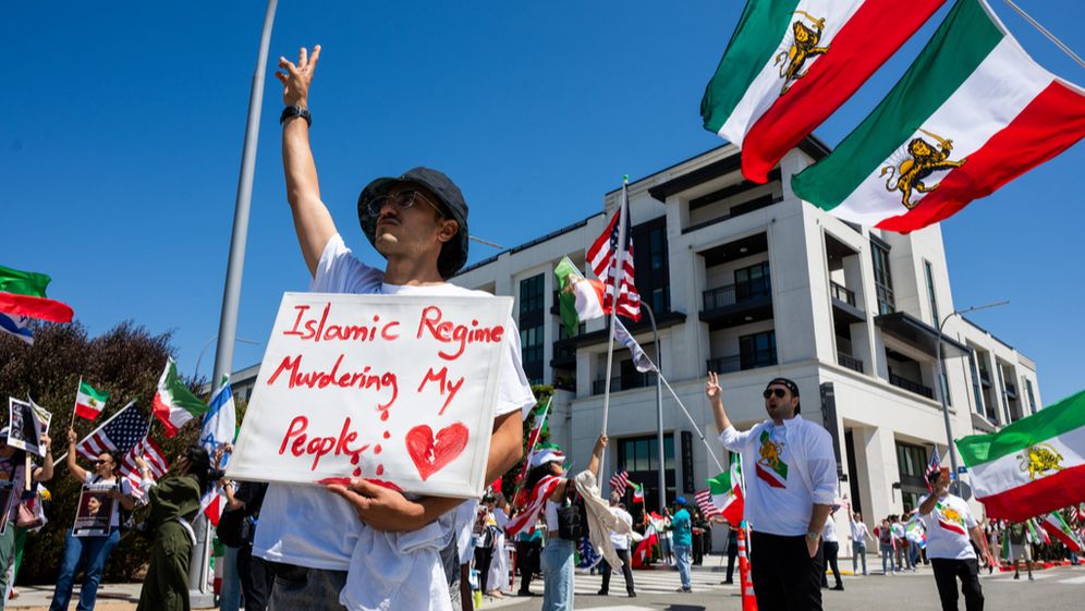 AP Photo/Benjamin Hanson Un homme brandit une pancarte sur laquelle on peut lire "Le régime islamique assassine mon peuple" lors d'une manifestation organisée en réaction à l'interdiction par la FIFA du drapeau pré-révolutionnaire de l'Iran