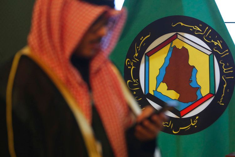 رجل ينظر إلى هاتفه المحمول أمام علم مجلس التعاون الخليجي في مدينة الكويت، الثلاثاء 5 ديسمبر/كانون الأول 2017