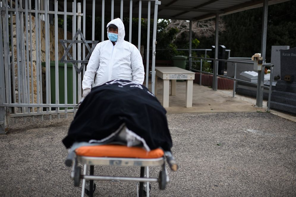Gili Yaari/Flash90 FILE - A burial services employee of 'Chevra Kadisha' carries the body of Romanian born Holocaust survivor Golda Schwartz who died at the age of 93 of Covid-19 in Nof Hagalil Cemetery, Israel, on January 28, 2021.