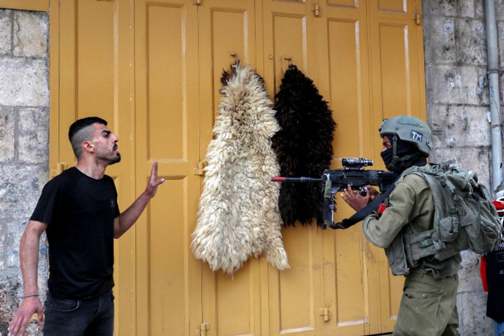 An Israeli soldier points his weapon at a Palestinian man during a protest, in the West Bank city of Hebron, on April 22, 2022.