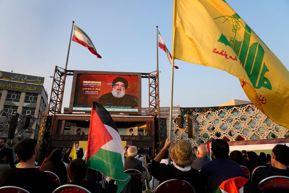 Manifestantes iranianos assistem a um discurso do secretário-geral do Hezbollah, Sayyed Hassan Nasrallah, enquanto seguram uma bandeira da organização terrorista designada.