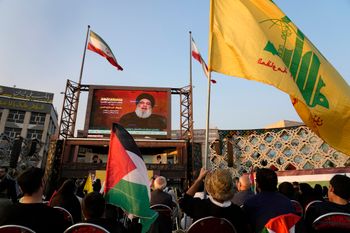 Iranian demonstrators watch a speech of Hezbollah Secretary-General Sayyed Hassan Nasrallah, while holding a flag of the designated terrorist organization.