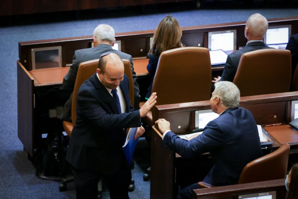 Naftali Bennett (walking) and Yair Lapid (sat down) greeting each other at the Knesset (Israel Parliament) session for the swearing-in of the new government, in Jerusalem on June 13, 2021.