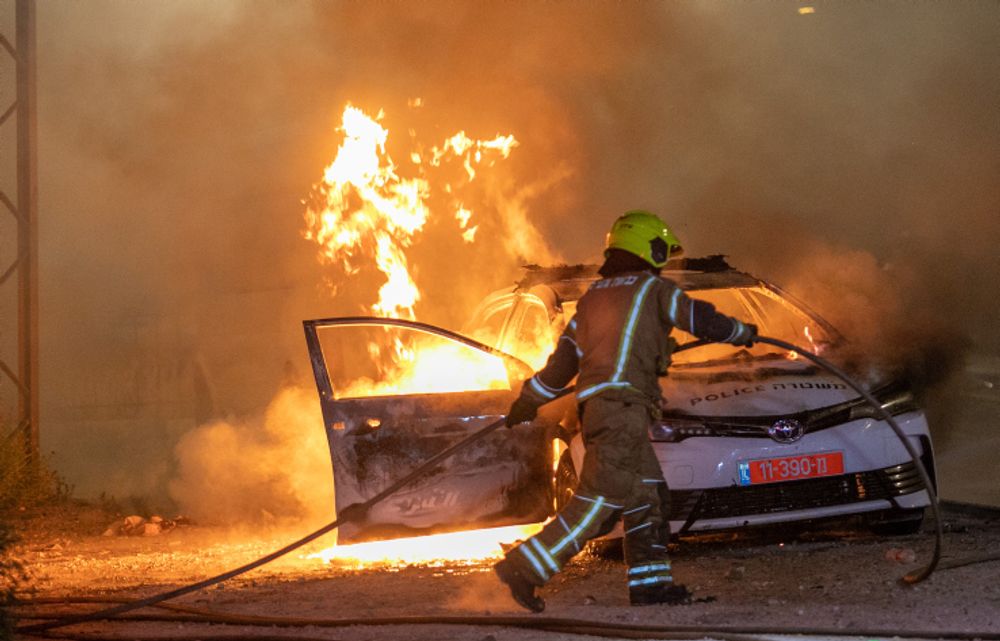 A firefighter works next to a burning police car, in the central city of Lod, May 12, 2021.