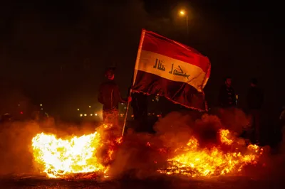 イラクの反政府抗議者は、2019年12月25日遅くにバスラ南部の都市の間に合わせの障害物に立ち向かう際に国旗を掲げています。