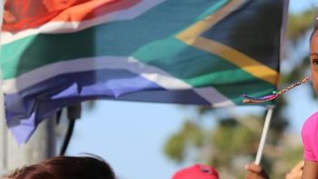 A girl looks on next to a man flying a South African flag as mourners gather to honour late South African president Nelson Mandela at an inter-faith service on December 6, 2013, held at the Grand Parade in Cape Town
