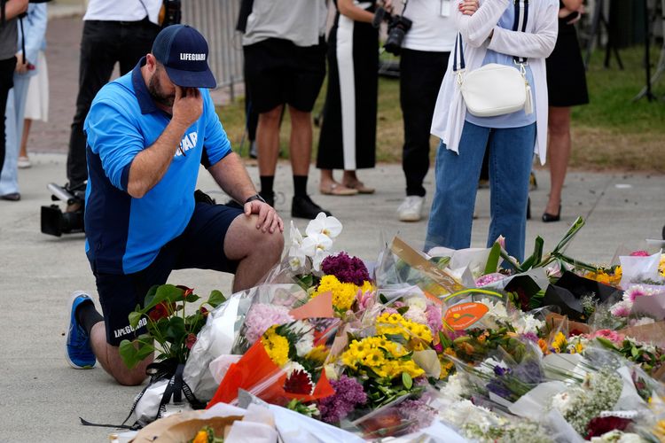 A lifeguard kneels to pay his respects at a floral memorial near the Bondi Pavilion at Bondi Beach on Tuesday, Dec. 16, 2025, following Sunday's shooting in Sydney, Australia
