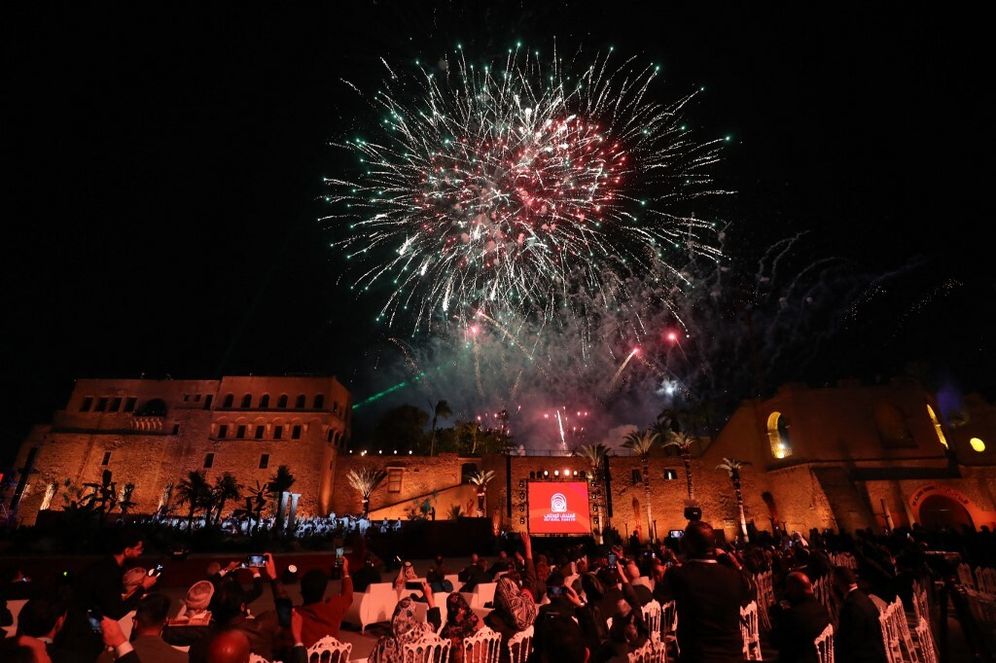 ينظر الناس إلى الألعاب النارية وهي تضيء السماء فوق القلعة الحمراء التاريخية (القلعة الحمراء) خلال حفل إعادة افتتاح المتحف الوطني في العاصمة الليبية طرابلس في 12 ديسمبر 2025.