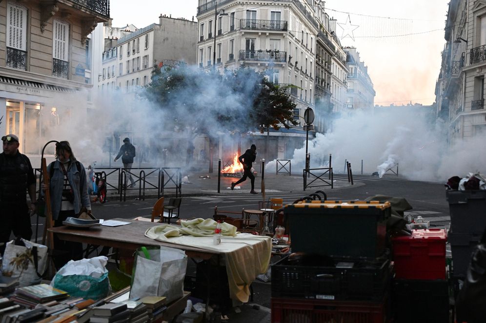Un manifestant court à travers un nuage de gaz lacrymogène alors qu’un marché aux puces se déroule pendant des affrontements entre manifestants et policiers à Paris, le dimanche 18 octobre 2026.
