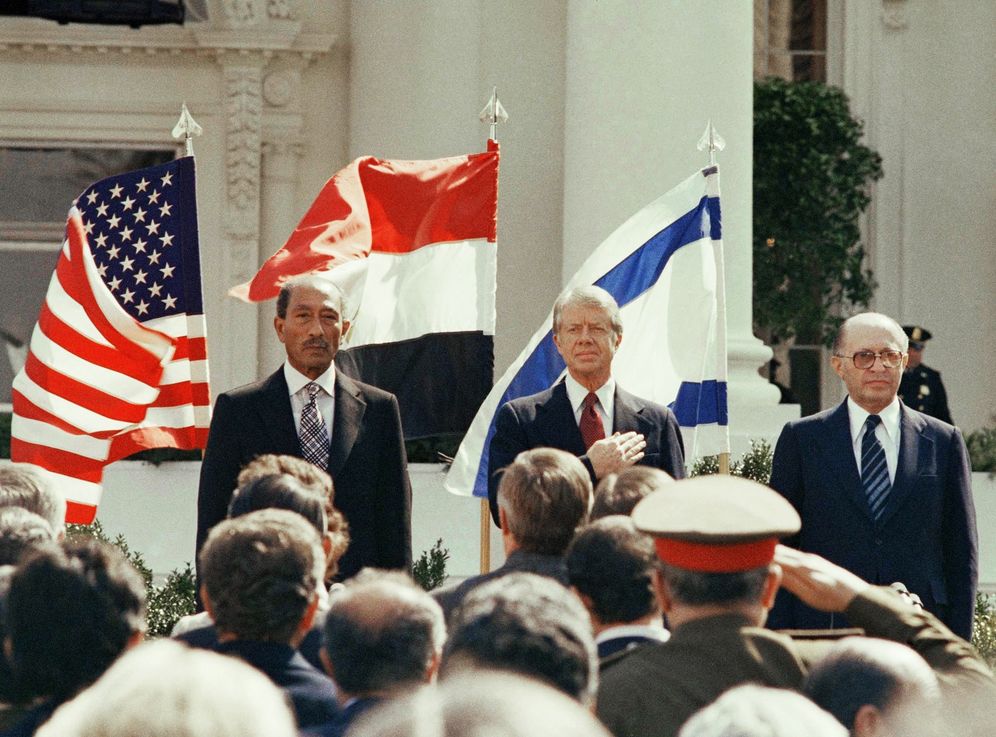 President Jimmy Carter stands in front of the billowing flags of Egypt, on the left, and Israel as the national anthems of the three countries are played before the signing of the peace treaty at the White House in Washington on March 26, 1979.