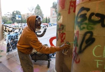 A demonstrator sprays graffiti on a building on the UCLA campus