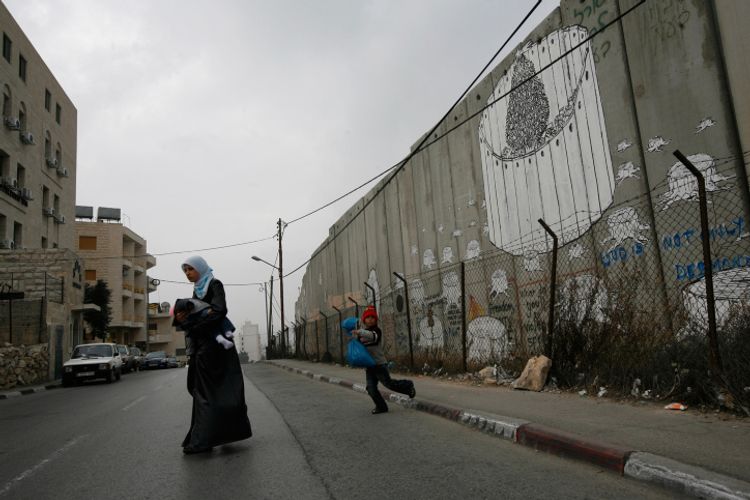 A woman crosses a street by the Separation Wall in the West Bank city of Bethlehem, on December 22, 2008.
