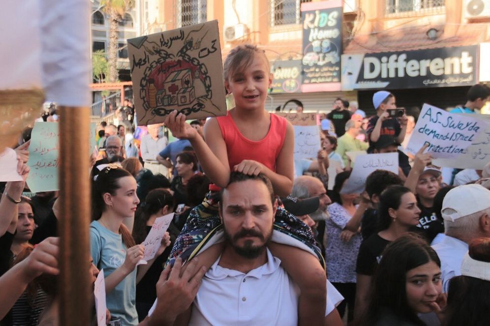 طفلة سورية تحمل لافتة خلال احتجاج على الوضع الإنساني في مدينة السويداء، في 28 يوليو/تموز 2025.