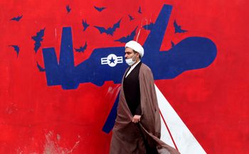An Iranian cleric walks past an anti-US mural on a wall of the former United States embassy in the capital Tehran, Iran, on March 12, 2022.