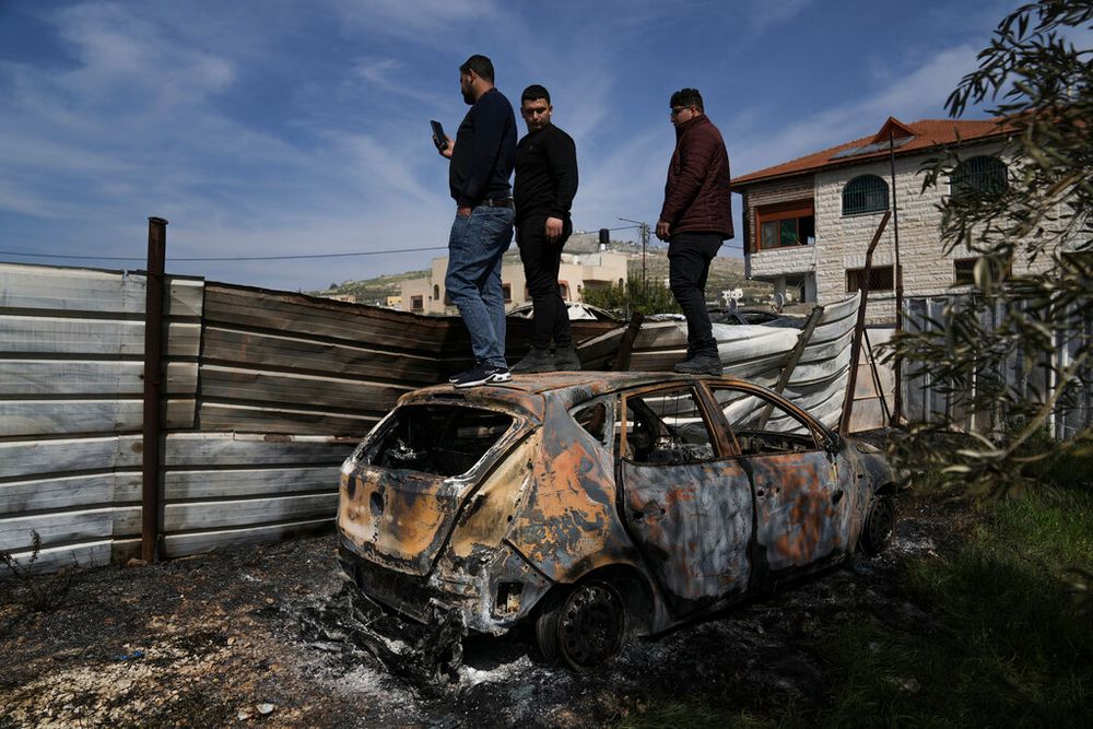 Palestinians stand on a scorched car to look at other damaged cars behind the fence in the town of Hawara, near the West Bank city of Nablus.