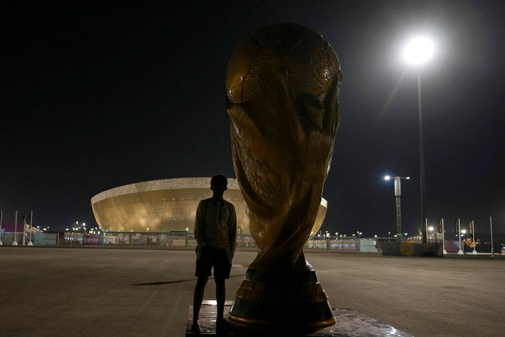 A man stands next to a replica of the World Cup in Doha, Qatar.