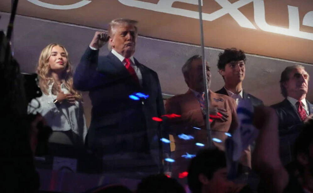 Mark Schiefelbein/AP US President Donald Trump gestures during the National Anthem as he attends an NBA Finals playoff basketball game between the New York Knicks and the San Antonio Spurs at Madison Square Garden in New York, June 8, 2026, with Kai Trump, left, Knicks owner James Dolan and Interior Secretary Doug Burgum, right.