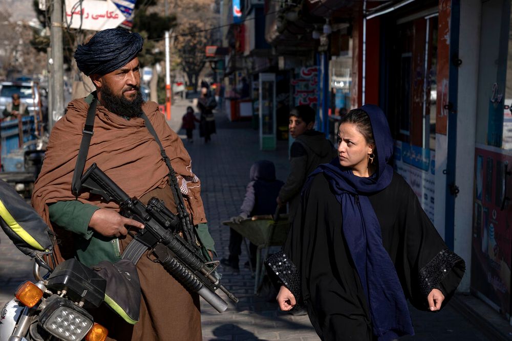 A Taliban fighter stands guard as a woman walks past in Kabul, Afghanistan.