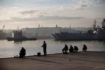 FILE - Local fishermen try to catch fish in front of Russia Navy ships in Sevastopol, Crimea.