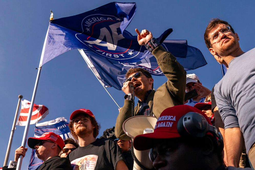 Nick Fuentes right-wing podcaster, center, speaks in front of flags that say, "America First," at a pro-Trump march.