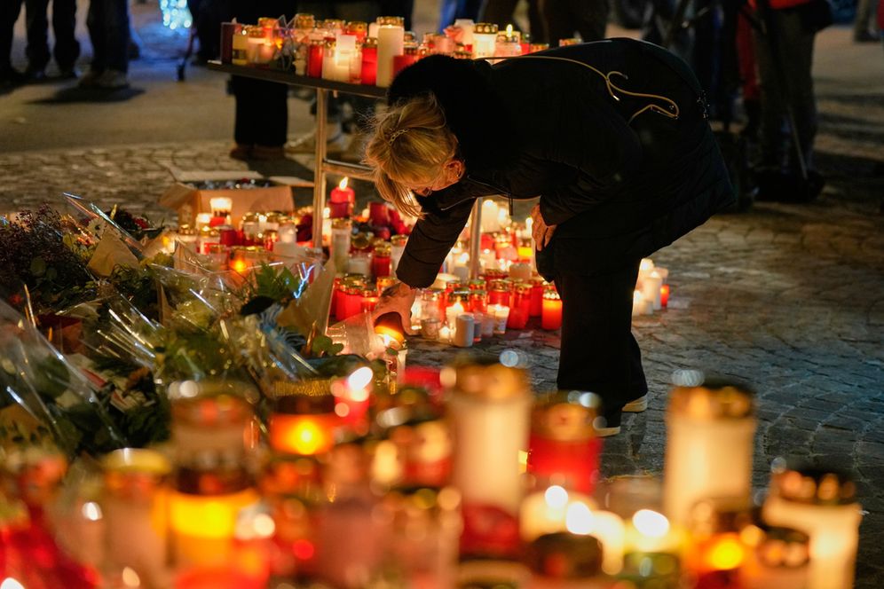 A woman lights a candle near the sealed off Le Constellation bar in Crans-Montana, Swiss Alps, Switzerland, Saturday, Jan. 3, 2026, where a devastating fire left dead and injured during the New Year's celebrations.