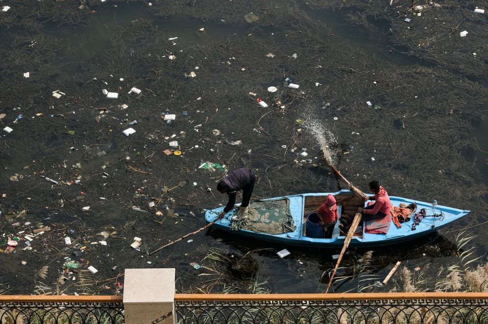 A man rows a fishing boat while another beats the water with a tree branch while cruising through the plastic-filled Nile River water off the shore in the Egyptian capital's twin city of Giza on February 13, 2022.