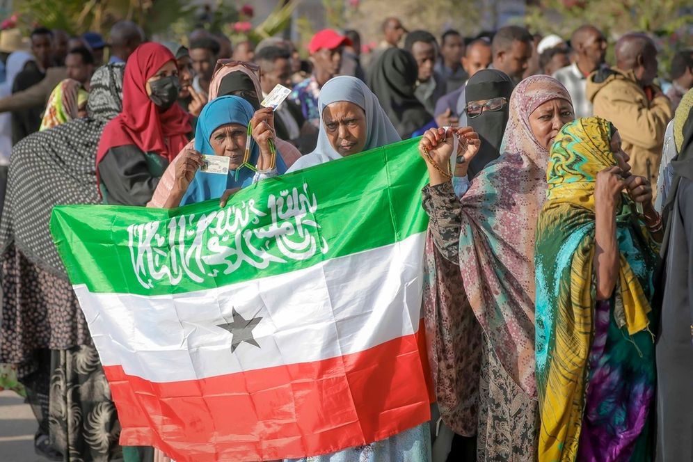 A woman displays the Somaliland flag as people queue to cast their votes during the 2024 Somaliland presidential election at a polling station in Hargeisa, Somaliland, Wednesday, Nov. 13,2024. 