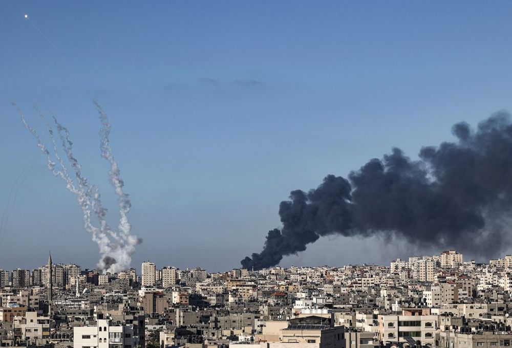 A plume of dark smoke rises above buildings hit by Israeli airstrikes in Gaza City, as rockets are fired (L) and intercepted by the Israeli Iron Dome missile defense system, on May 15, 2021.