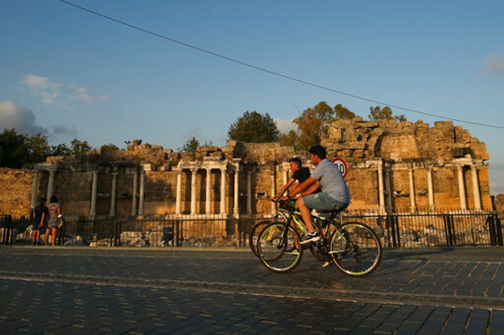 Tourists ride their bicycles in front of an ancient site in Antalya, southern Turkey, on June 20, 2021.