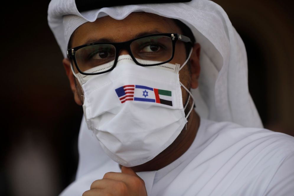 Nir Elias / Pool Photo via AP 2020 © A man wearing a mask bearing the national flags of America, Israel and United Arab Emirates, watches a ceremony after an El Al plane from Israel landed in Abu Dhabi, United Arab Emirates, on Aug. 31, 2020.