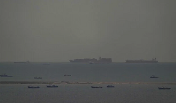 Des bateaux de pêche parsèment la mer tandis que, à l’arrière-plan, des navires marchands naviguent dans le golfe Arabo-Persique en direction du détroit d’Ormuz, au large des Émirats arabes unis, le 27 mars 2026. 