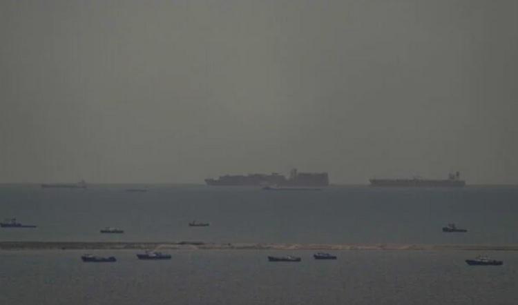 Des bateaux de pêche parsèment la mer tandis que, à l’arrière-plan, des navires marchands naviguent dans le golfe Arabo-Persique en direction du détroit d’Ormuz, au large des Émirats arabes unis, le 27 mars 2026. 