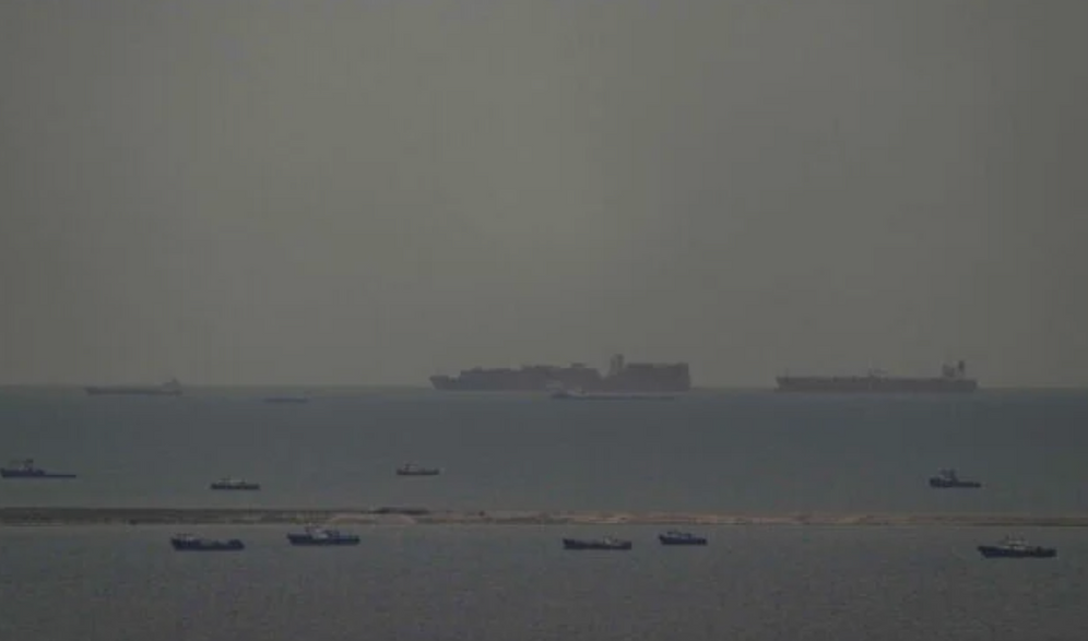 Des bateaux de pêche parsèment la mer tandis que, à l’arrière-plan, des navires marchands naviguent dans le golfe Arabo-Persique en direction du détroit d’Ormuz, au large des Émirats arabes unis, le 27 mars 2026. 