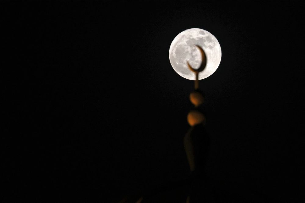 The full moon rises behind a minaret in Dubai, the United Arab Emirates, on June 14, 2022.